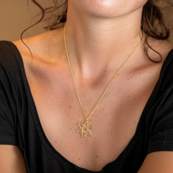 Close-up of a woman wearing the gold vermeil atom necklace, the pendant resting at her chest, highlighting its delicate scientific design and subtle shine.