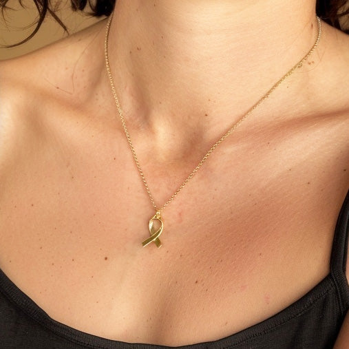 Close-up view of the gold vermeil awareness ribbon necklace resting on a woman’s collarbone, paired with a thin gold chain.