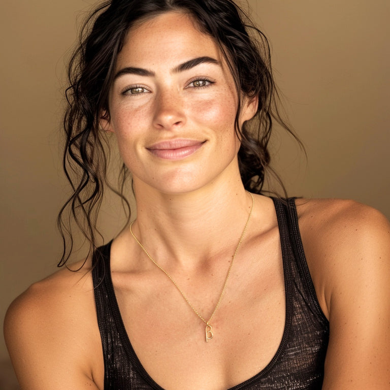 Smiling woman with dark wavy hair wearing the gold vermeil beta necklace against a golden-brown background.