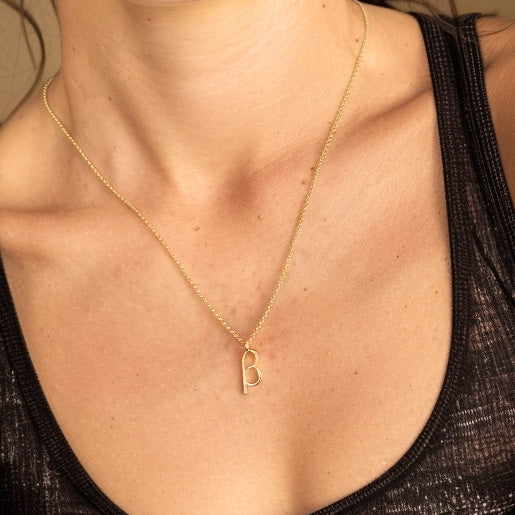 Close-up of a woman wearing the gold vermeil beta necklace, the beta pendant resting on her chest.