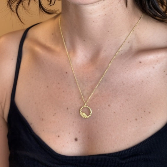 Close-up of a woman wearing the gold vermeil blastocyst necklace, showing the pendant resting on her chest against a black top.