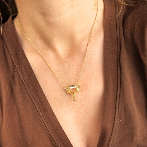 Close-up of a person’s neck and upper chest wearing the cervical vertebra necklace in gold vermeil on a delicate chain, paired with a brown V-neck top.