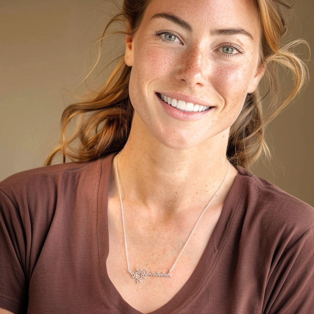 Smiling woman with light skin and brown hair wearing a brown shirt, showcasing the silver chlorophyll molecule necklace.