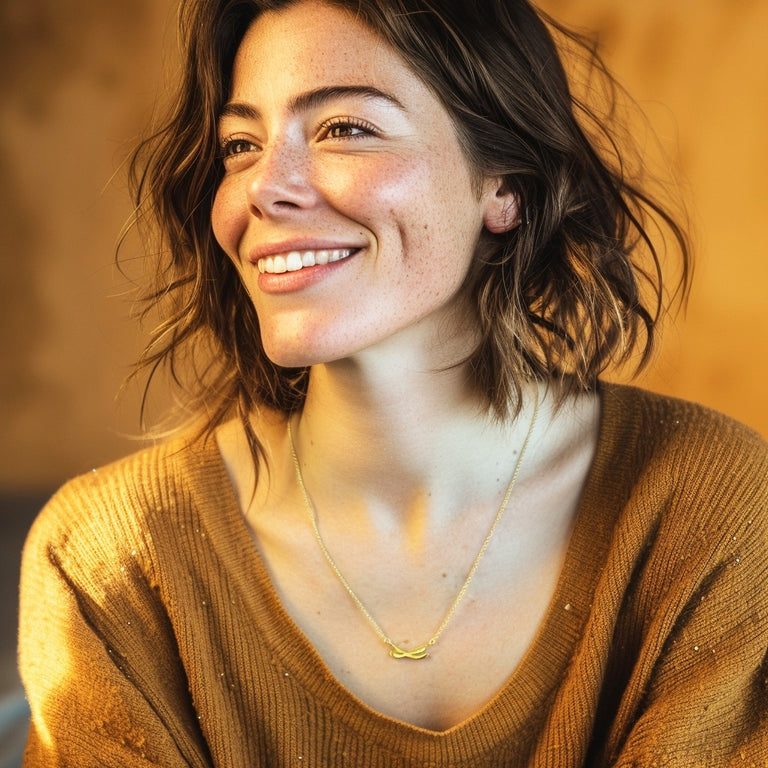Smiling woman wearing a gold vermeil chromosome necklace, photographed from the shoulders up in warm natural light.