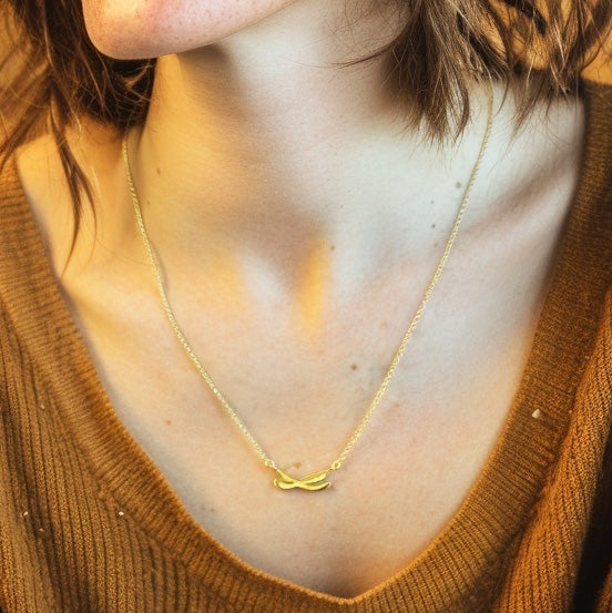 Close-up of a woman’s neck and collarbone showing the gold vermeil chromosome necklace resting on her skin.