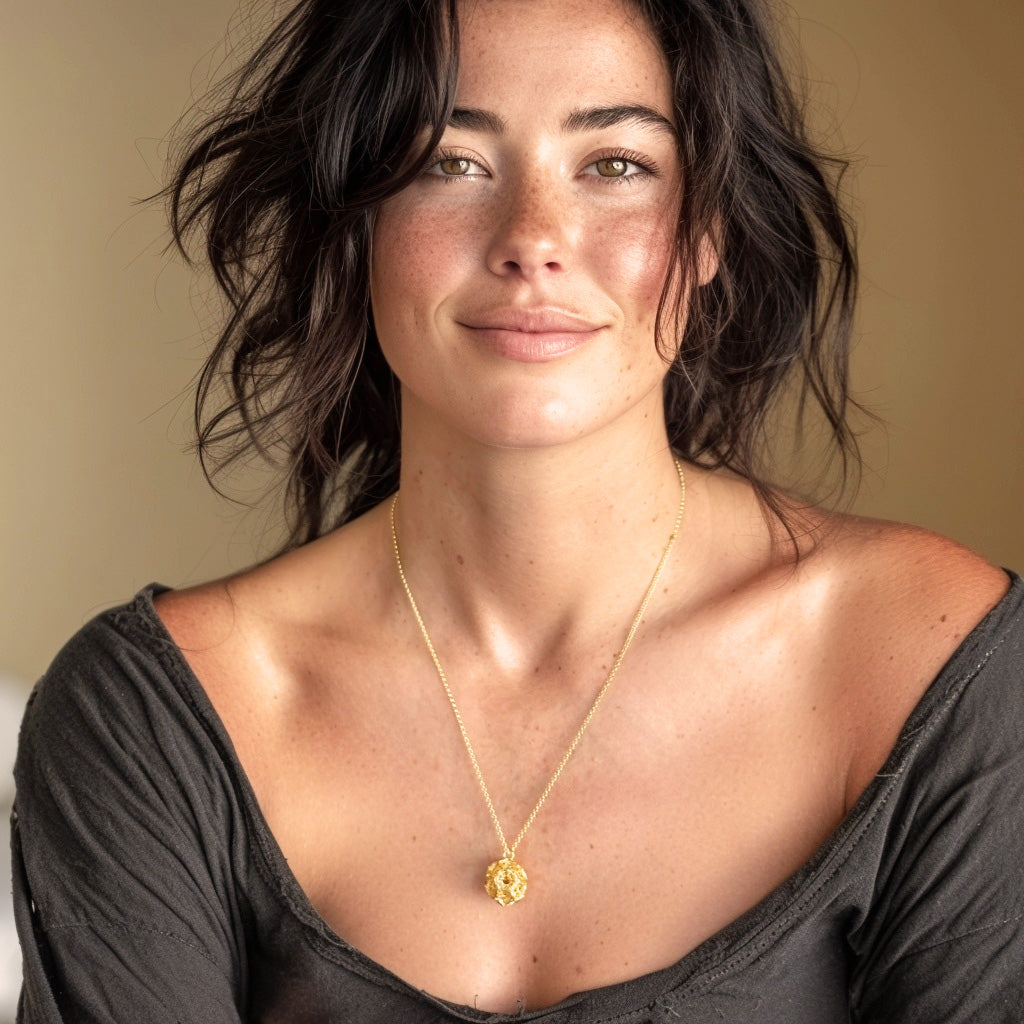 Woman wearing the Gold Vermeil Clathrin Necklace, showcasing the molecular-inspired pendant styled with a low-cut dark top.