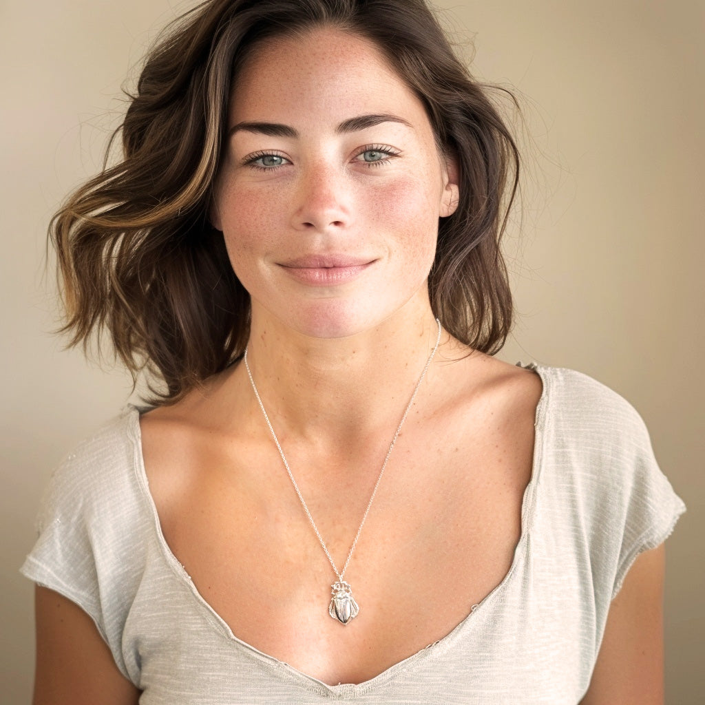 Woman wearing the cockchafer necklace over a light beige V-neck shirt, smiling softly at the camera.