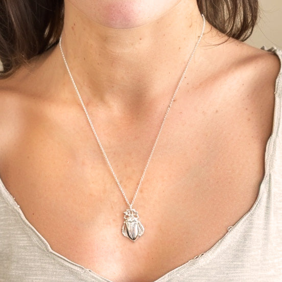 Close-up of the cockchafer necklace worn by a woman, highlighting the silver beetle pendant against her neckline.