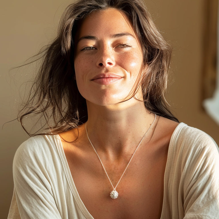 Smiling woman with long dark hair wearing a white blouse and the sterling silver coronavirus necklace, captured in warm natural light.