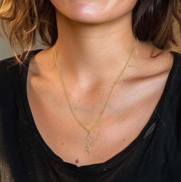 Close-up of a woman’s neck and collarbone wearing the gold vermeil cortisol molecule necklace against a black shirt.