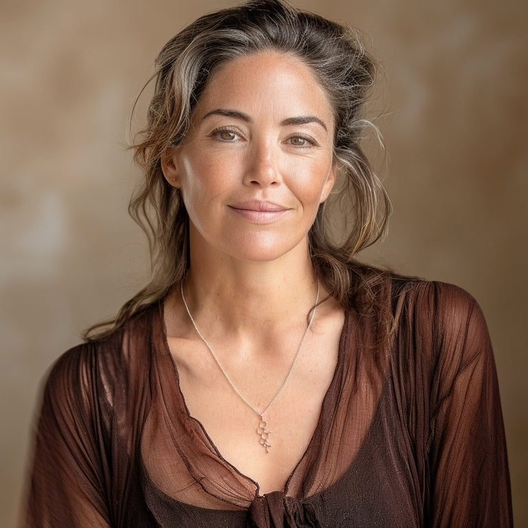 Smiling woman wearing a brown top and the cortisol molecule necklace, shown in a warm-toned studio portrait.
