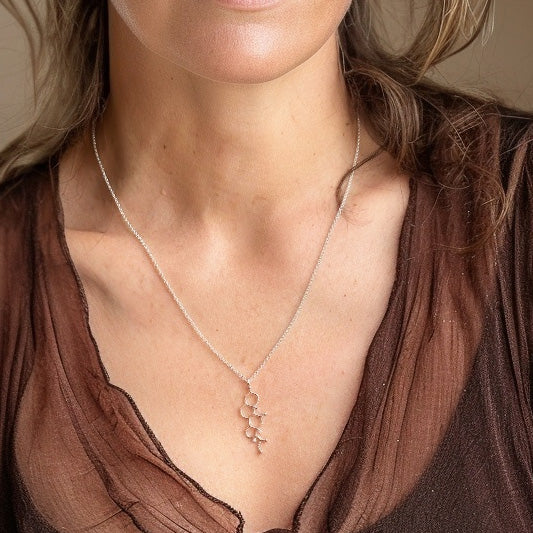 Close-up of a woman wearing the cortisol molecule necklace over a brown blouse.