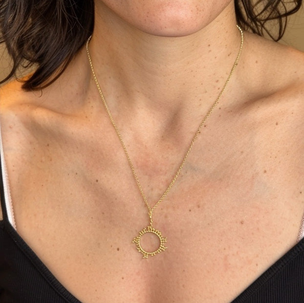 The cyclosporine gold necklace worn around a woman’s neck, resting on bare skin with a black top, showing the pendant’s size and delicate chain.