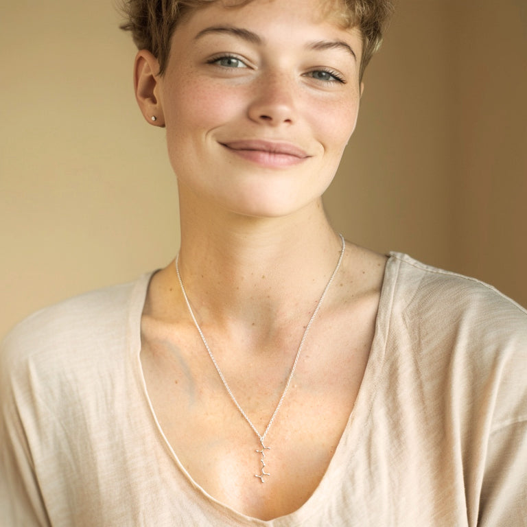 Smiling woman wearing a sterling silver cystine necklace with a double-layered chain, styled casually with a light beige top.