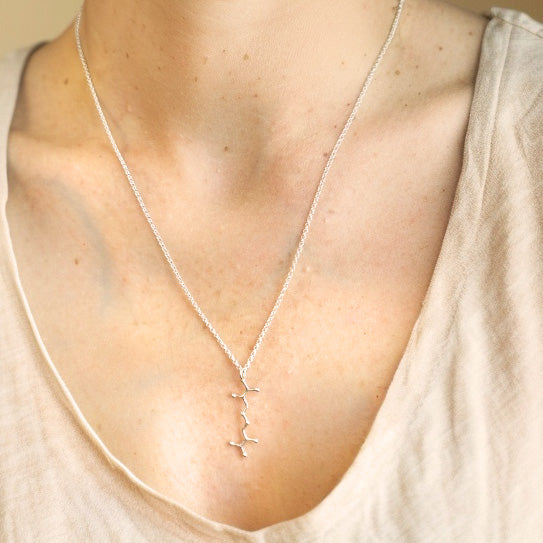 Close-up view of the sterling silver cystine necklace resting on the chest of a woman wearing a light beige V-neck shirt.
