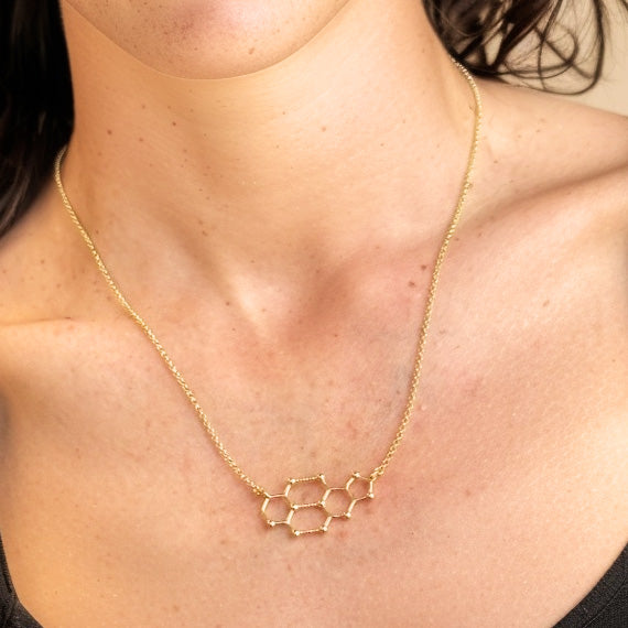 Close-up of cytosine–guanine DNA base pair necklace in gold vermeil on model’s neck, elegant science jewelry gift