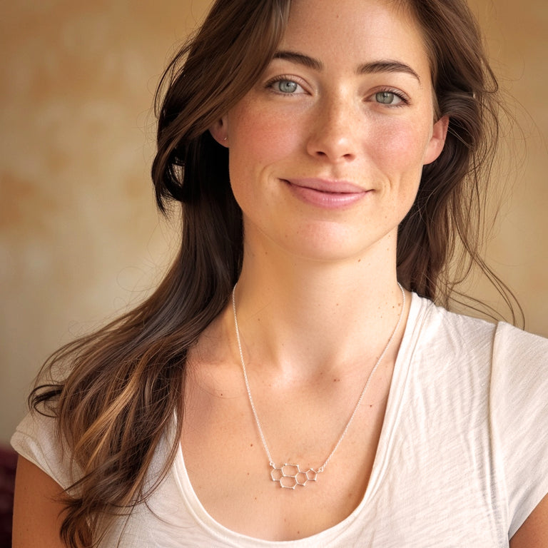 Smiling woman with long brown hair wearing a white shirt and the cytosine–guanine necklace, showing how it looks when worn.