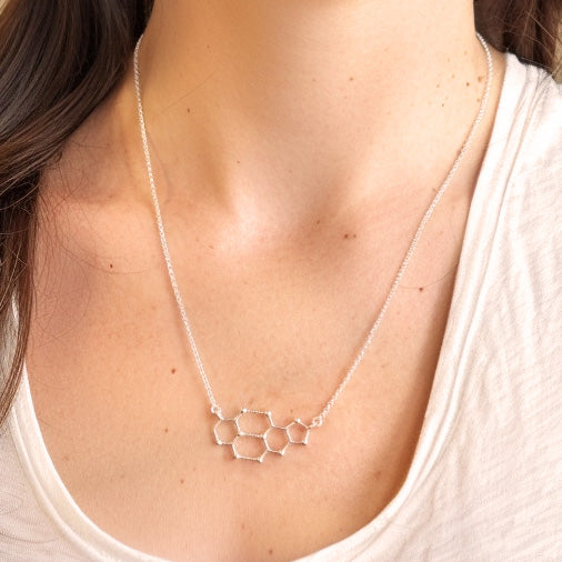 The cytosine–guanine necklace worn by a person, resting just below the collarbone on a white shirt.