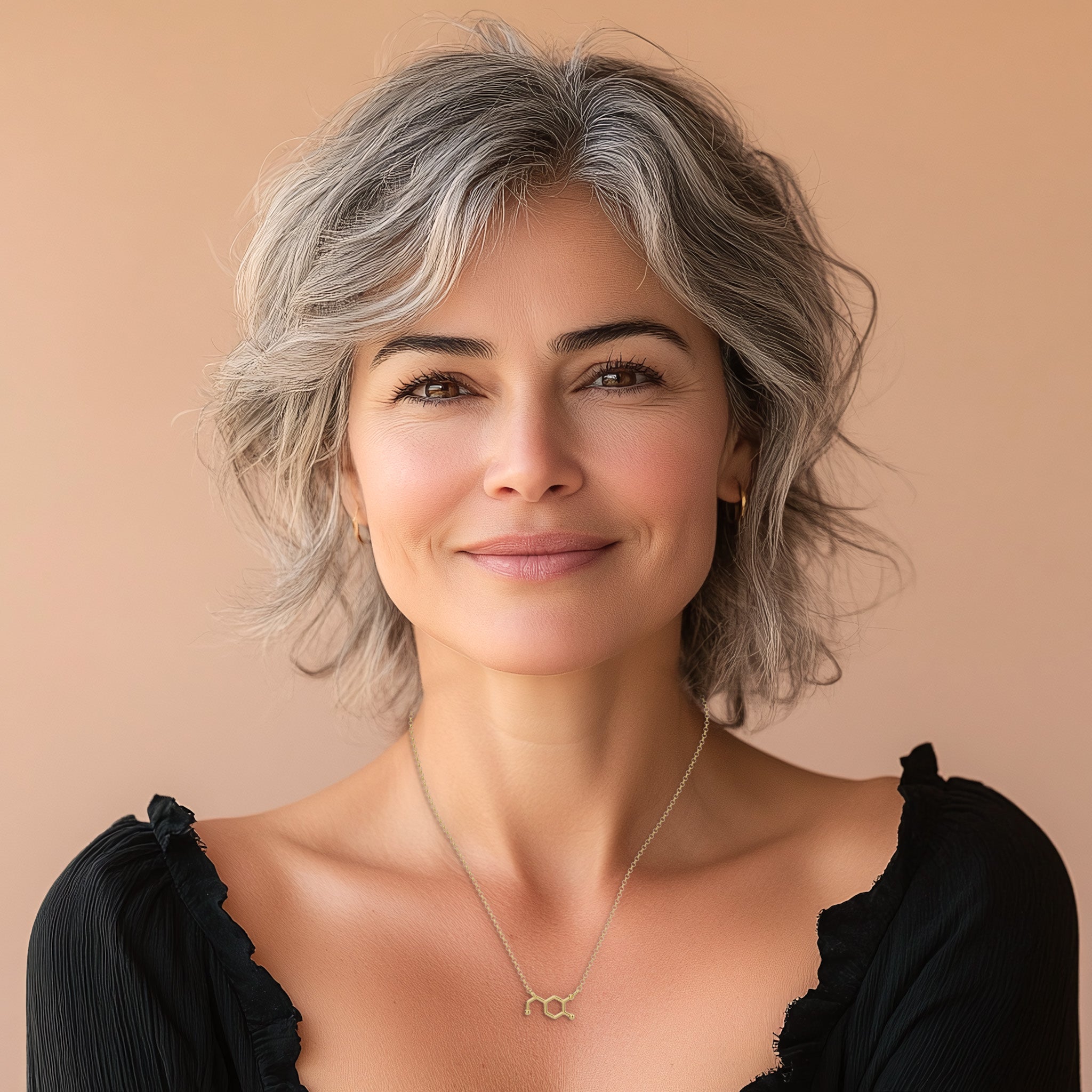 A woman with shoulder-length hair, wearing a dopamine molecule necklace in gold vermeil. The necklace sits gracefully on her neck, highlighting its dainty and elegant style. The model is dressed in a simple black top, emphasizing the necklace as the focal point.