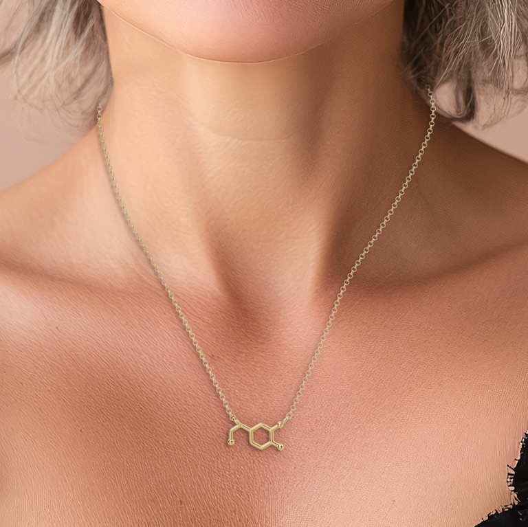 A close-up of a woman’s neck with the dopamine molecule necklace in gold vermeil. The necklace’s fine detail and shiny finish are visible, drawing attention to the molecular design. The image focuses on the necklace, showing its size and fit on the neck.