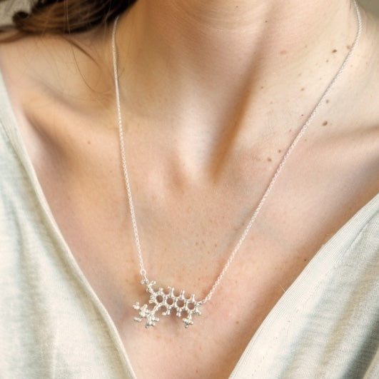 Close-up view of a sterling silver doxorubicin molecule necklace resting on a woman’s chest, highlighting the intricate molecular design.