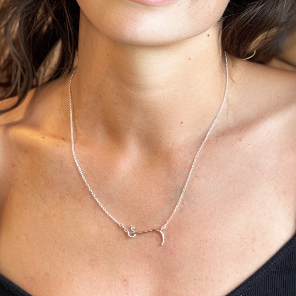 Close-up view of the Ebola virus pendant necklace on model’s neck, showing the curved viral filament in polished silver. A subtle, conversation-starting piece of science jewelry merging virology and art.