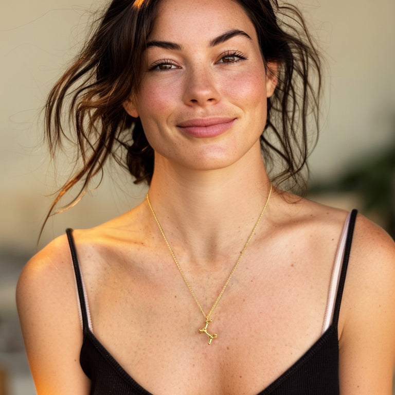 Smiling woman with wavy hair wearing a black spaghetti strap top, showcasing the gold vermeil ethanol molecule necklace layered around her neck.