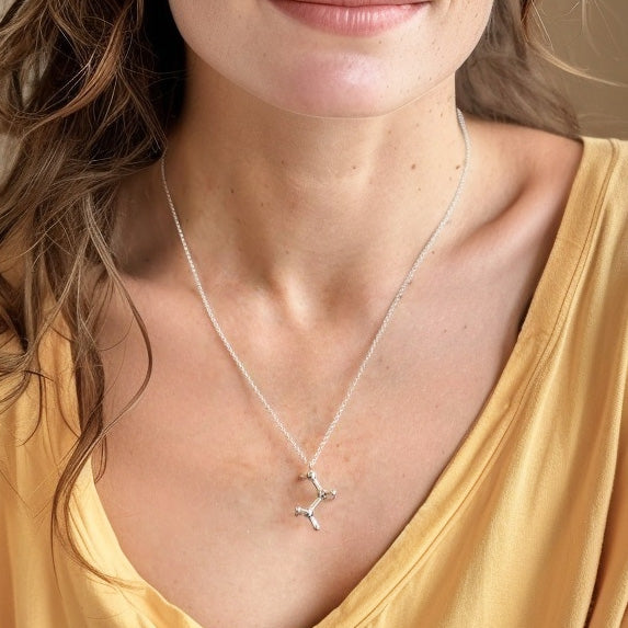 Close-up of a woman wearing the ethanol molecule necklace, showing the pendant resting just below the collarbone.