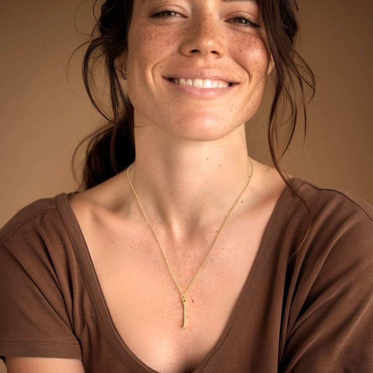 A smiling woman wearing the gold femur necklace over a brown top, the pendant hanging at chest level and catching the light.