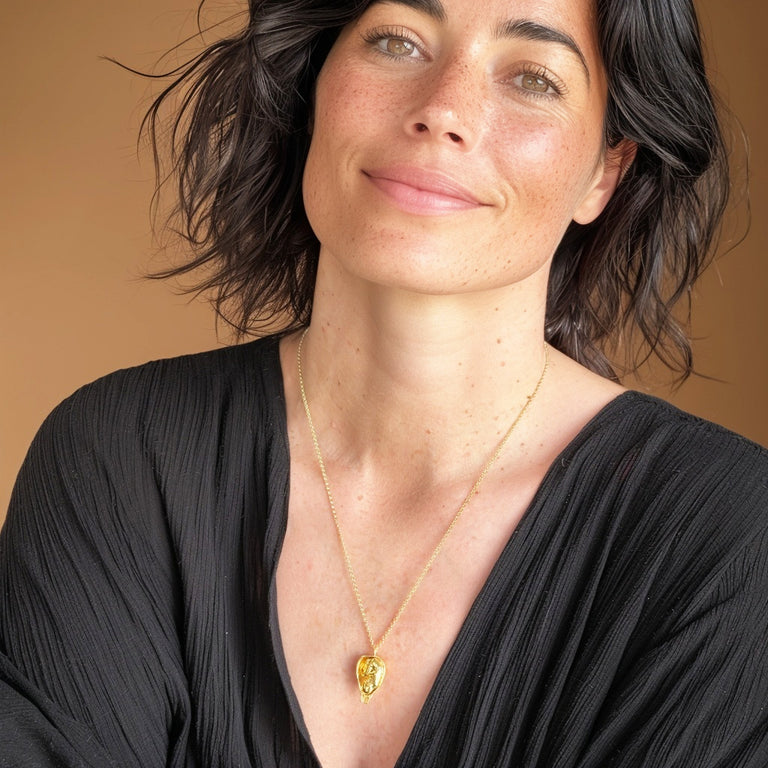 Smiling woman wearing the gold vermeil fetus necklace, pendant resting at mid-chest, styled with a black v-neck top.