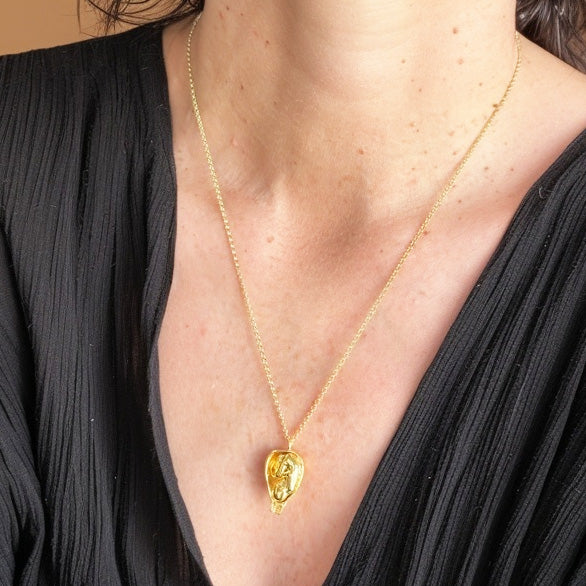 Close-up of the gold vermeil fetus necklace worn on the chest, showing the detailed pendant design against a black top.