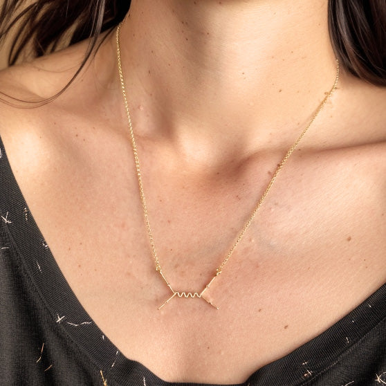 Woman wearing the Feynman Scattering Necklace in gold vermeil, showing the particle physics design resting elegantly on her collarbone.