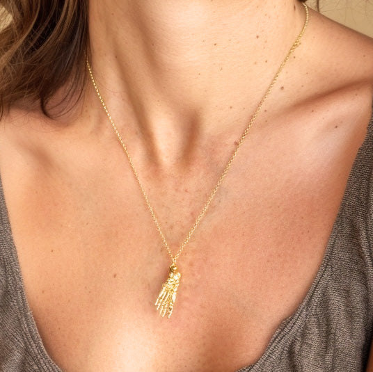 Close-up of a woman wearing the gold vermeil foot anatomy necklace on a fine gold chain around her neck.