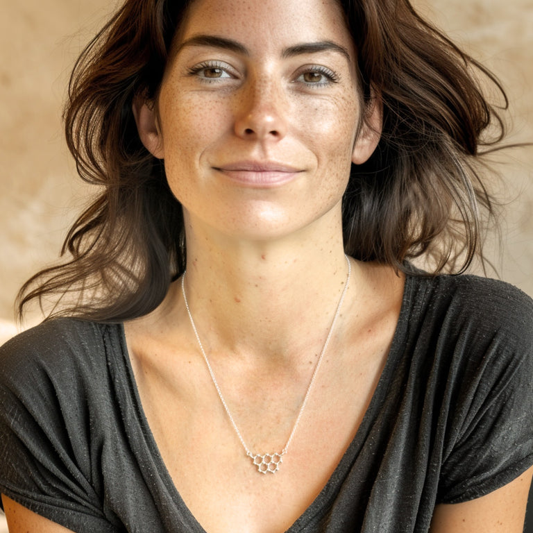 Woman wearing the silver graphite necklace against a dark grey V-neck shirt, smiling softly while showing the necklace clearly.