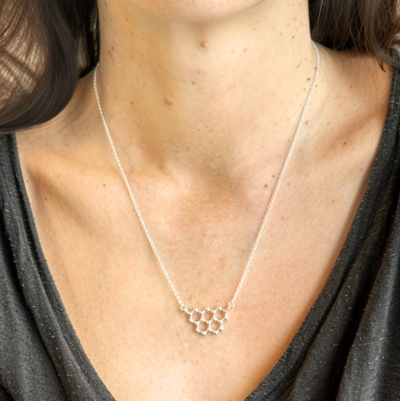 Close-up of the silver graphite necklace worn on a woman’s neck with a dark grey shirt, focusing on the pendant’s hexagonal lattice design.