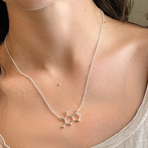 Close-up of guanine molecule necklace resting on collarbone, elegant science-inspired jewelry