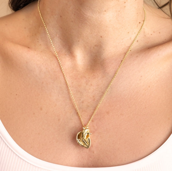 Close-up view of a gold vermeil anatomical heart section necklace resting on a woman’s chest, highlighting the anatomical detail.