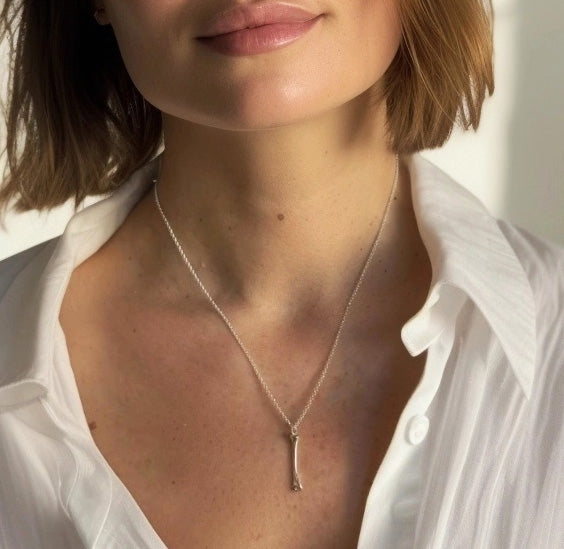 Woman wearing a silver humerus bone necklace over a crisp white shirt, showcasing the pendant’s sleek and minimalist design.