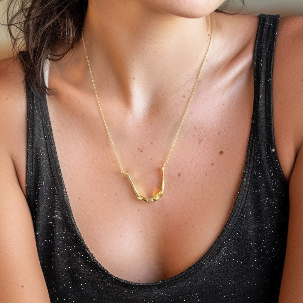 Close-up of the vermeil gold hyoid bone necklace worn around the neck, showing its smooth curvature and subtle shine against a dark glittery top.