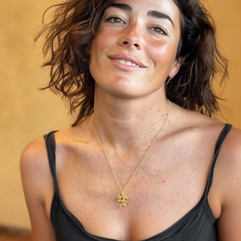 Portrait of a smiling woman with short brown hair wearing the juniper molecule necklace in gold vermeil, photographed in warm lighting for a natural, stylish look.