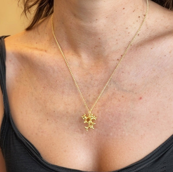 Woman wearing the gold vermeil juniper molecule necklace against bare skin and a black tank top, showing the pendant’s size and elegant shine.