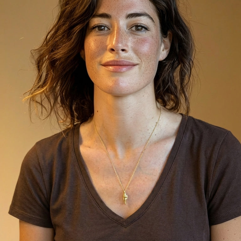 Woman smiling while wearing a gold knee-joint necklace over a brown V-neck shirt.