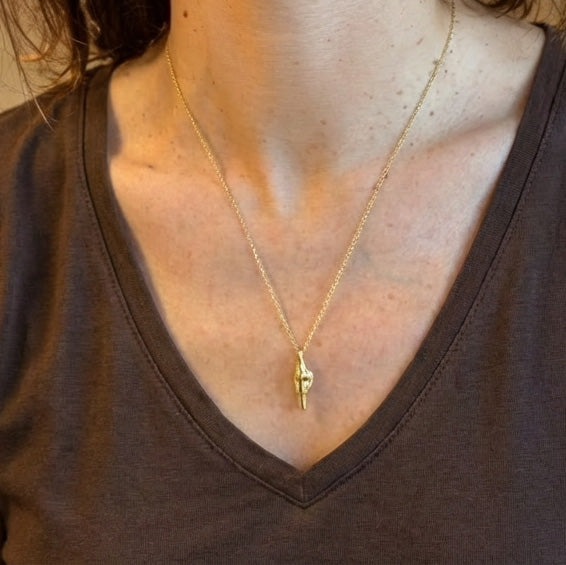 Close-up of a woman wearing a gold knee-joint necklace over a brown V-neck shirt.