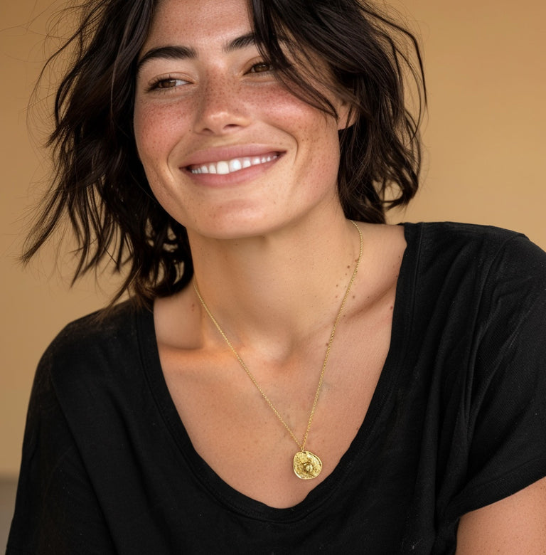 Smiling woman wearing the gold vermeil mammalian cell necklace with a black top, highlighting how the pendant rests naturally and catches light.