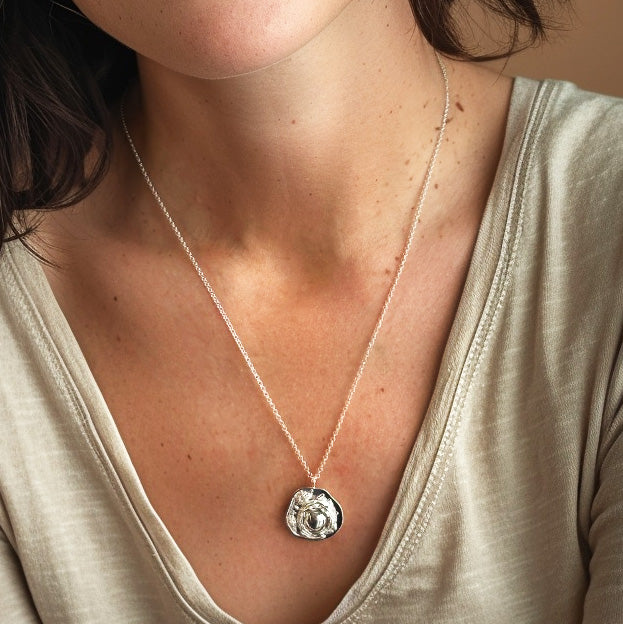 Close-up of the mammalian cell necklace worn by a woman, highlighting the pendant’s size and detailed design against her skin and clothing
