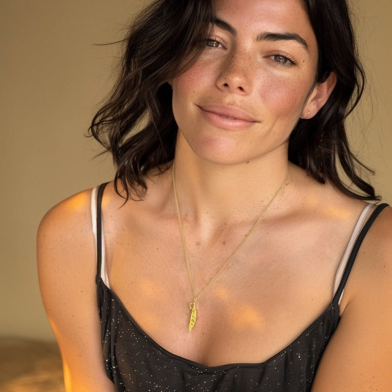 Model wearing the Mendel’s peas necklace in gold vermeil with a black top, smiling softly in a warm-toned studio setting.