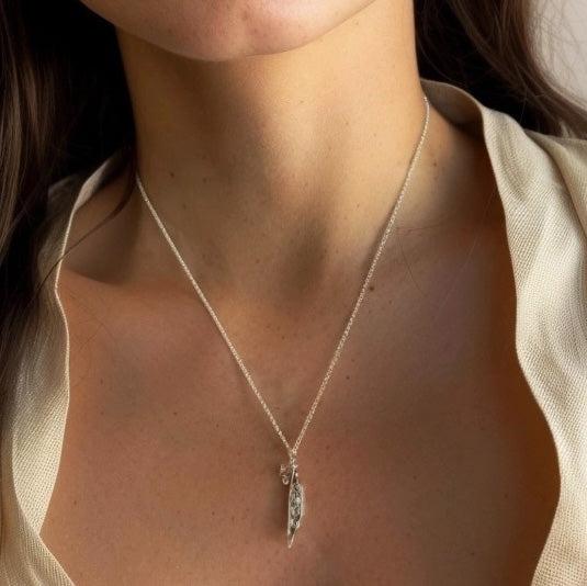 Close-up of a woman wearing the Mendel’s Peas Necklace, the silver pea pod pendant resting elegantly just below the collarbone.