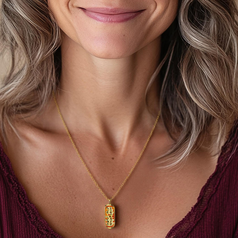 A close-up of a woman’s neck showcasing the gold vermeil mitochondrion necklace. The pendant dangles gracefully from a delicate chain, resting just above her collarbone. The fine details of the necklace are clearly visible, highlighting its intricate design and scientific inspiration.