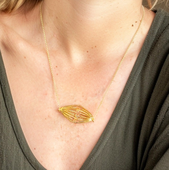 Close-up of a gold vermeil mitosis necklace resting on the chest of a person wearing a V-neck green top.