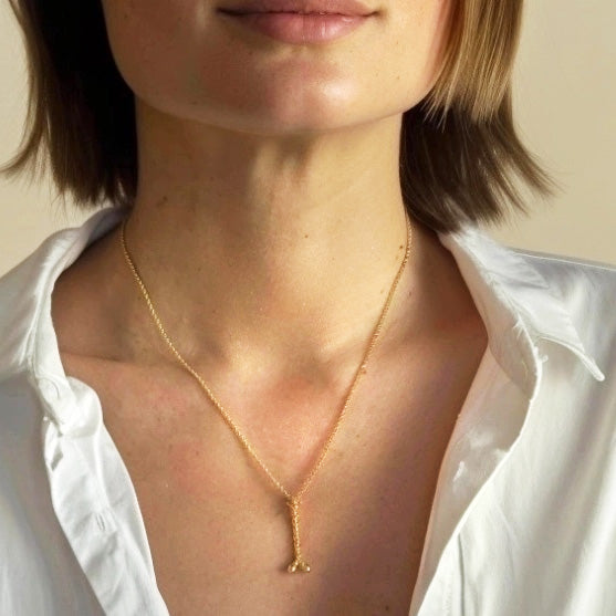 Close-up of a woman wearing a gold vermeil myosin necklace, paired with an open white shirt, emphasizing the necklace’s delicate and scientific design.